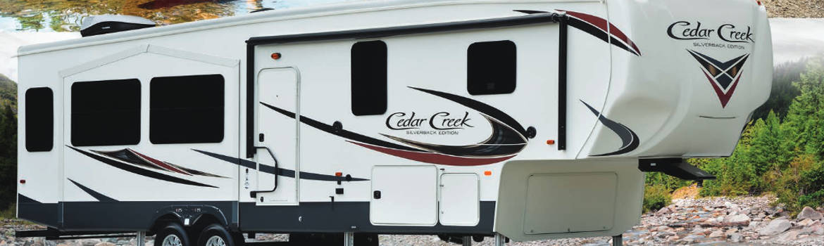 A white 2018 Cedar Creek Silverback fifth wheel parked next to a lake.